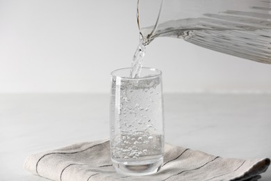 Photo of Pouring water from jug into glass on white table indoors