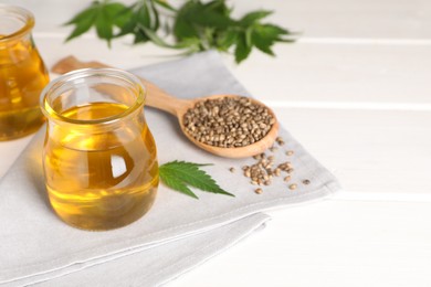 Photo of Hemp oil, fresh leaves and seeds on white wooden table. Space for text