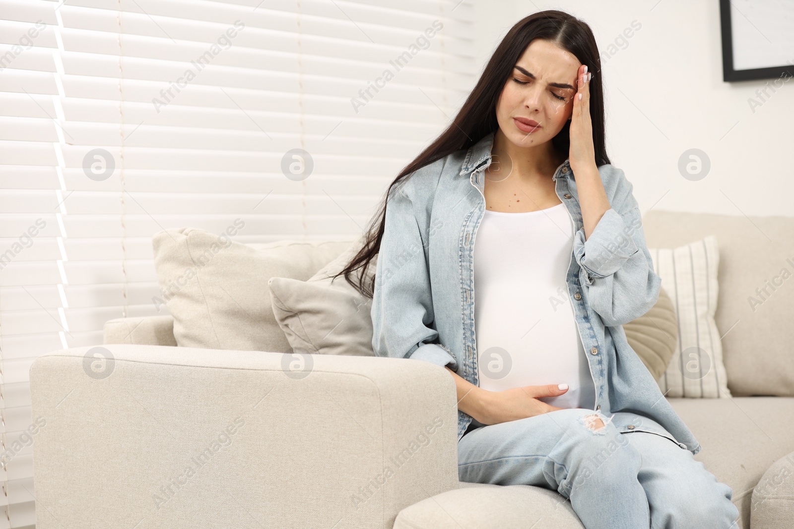 Photo of Pregnant woman suffering from headache on sofa at home