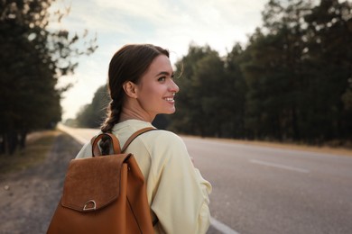 Young woman with backpack on road near forest