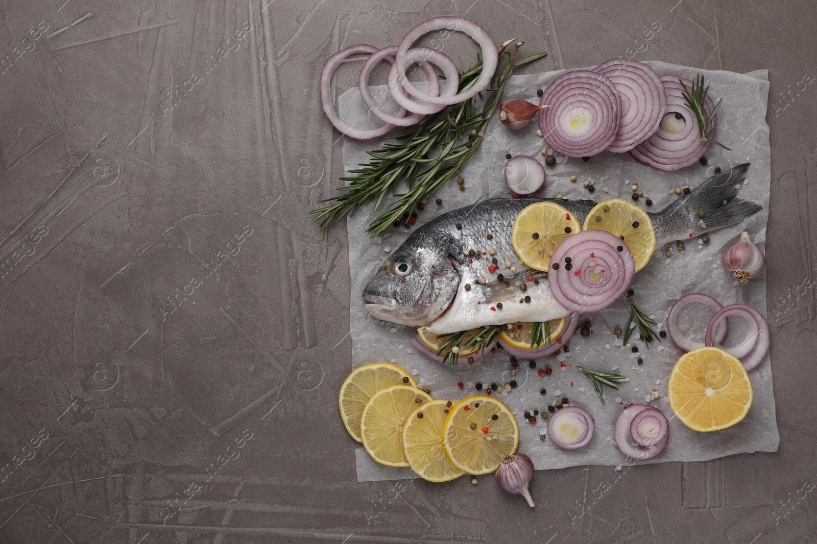 Photo of Raw dorado fish with spices, lemon and onion on grey textured table, top view. Space for text