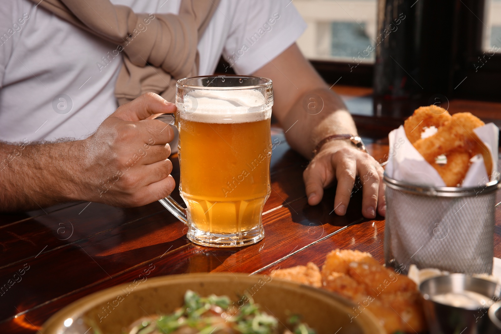 Photo of Man with glass of tasty beer at wooden table in pub, closeup