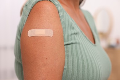 Woman with adhesive bandage on her arm after vaccination against blurred background, closeup