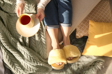 Woman with cup of tea wearing soft comfortable slippers at home, top view