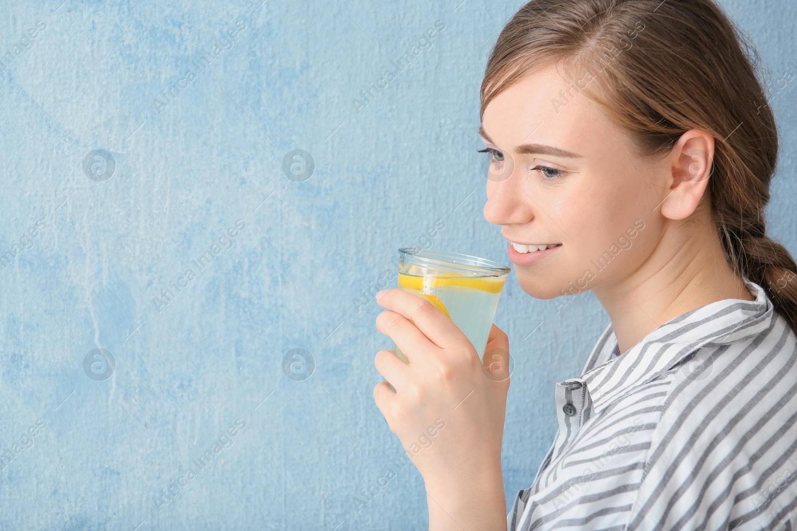 Photo of Young woman drinking water with lemon against color background