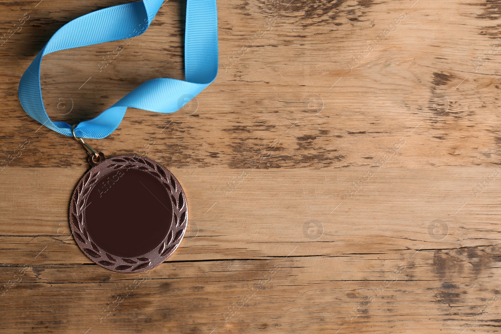 Photo of Bronze medal with light blue ribbon on wooden background, flat lay. Space for design