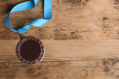 Photo of Bronze medal with light blue ribbon on wooden background, flat lay. Space for design