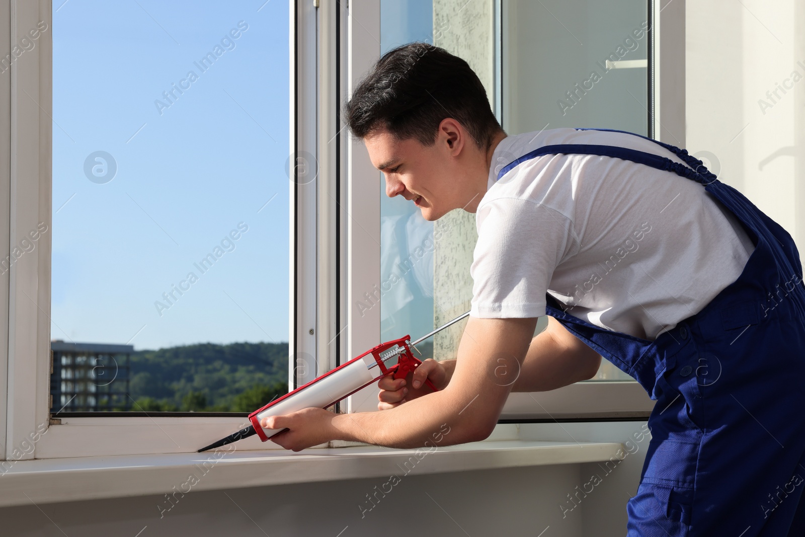 Photo of Worker sealing plastic window with caulk indoors. Installation process