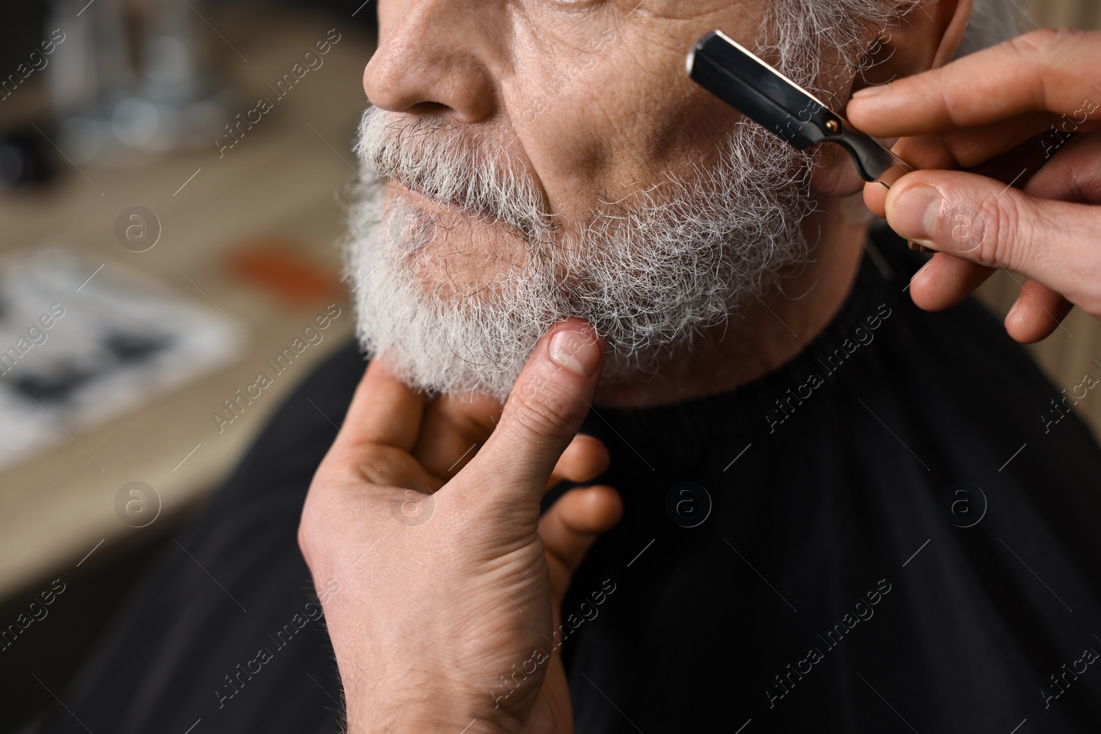 Photo of Professional barber shaving client's beard with blade in barbershop, closeup