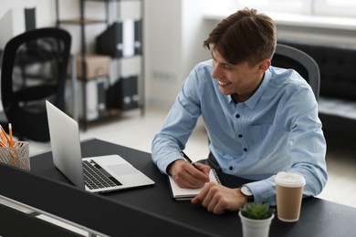 Photo of Man taking notes during webinar at table in office