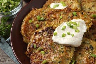 Photo of Delicious zucchini pancakes with sour cream and green onion in bowl, closeup
