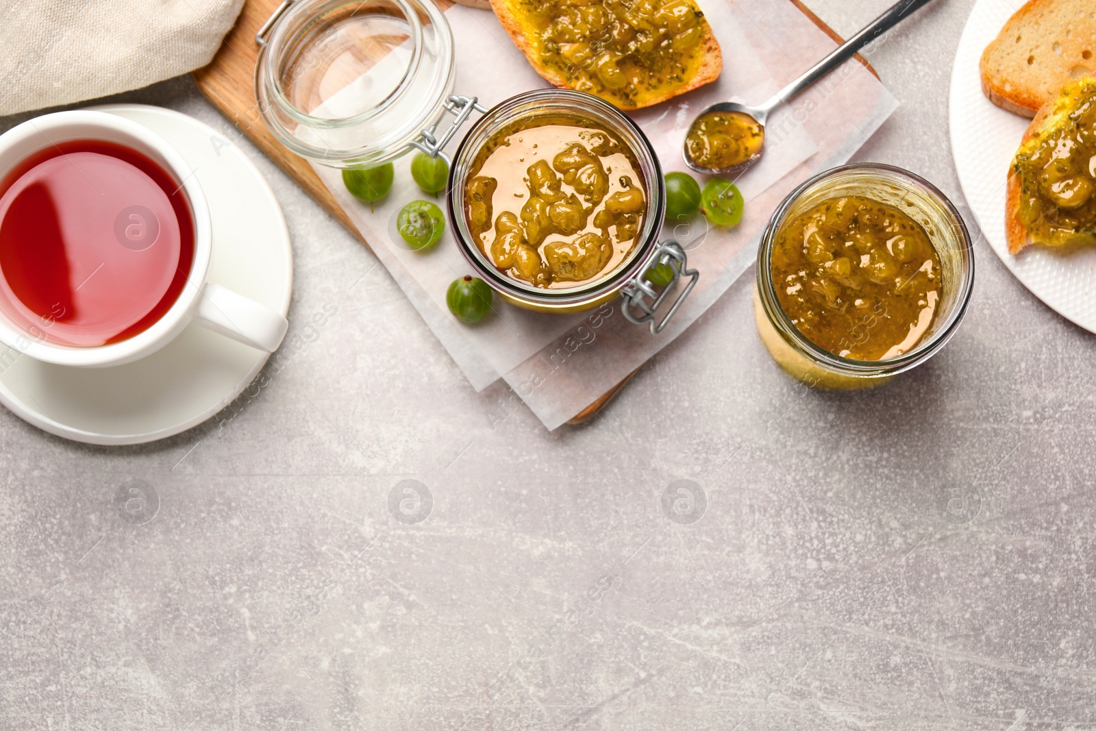 Photo of Delicious gooseberry jam, fresh berries and tea on grey table, flat lay. Space for text