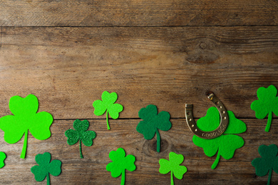 Photo of Flat lay composition with clover leaves and horseshoe on wooden background, space for text. St. Patrick's day