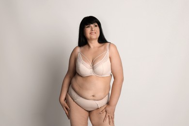 Beautiful overweight woman in beige underwear on light background. Plus-size model