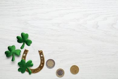 Golden horseshoe, decorative clover leaves and coins on white wooden table, flat lay with space for text. Saint Patrick's Day celebration