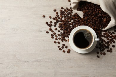 Photo of Cup of aromatic coffee and beans on light wooden table, flat lay. Space for text
