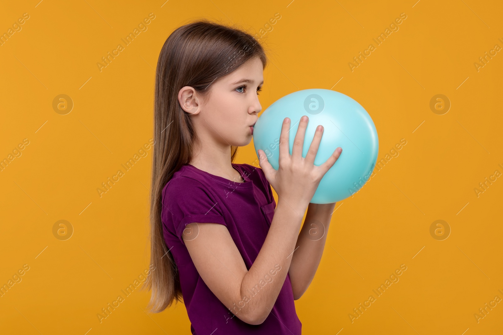 Photo of Girl inflating bright balloon on orange background