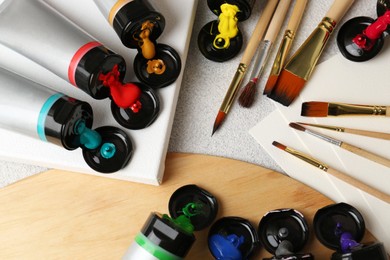 Photo of Tubes of colorful paints and brushes on textured table, flat lay