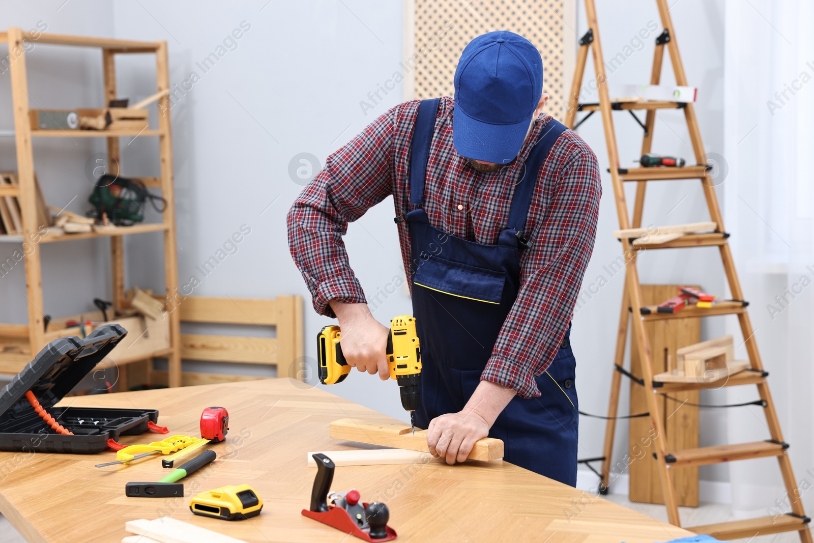 Photo of Young worker using electric drill at table in workshop