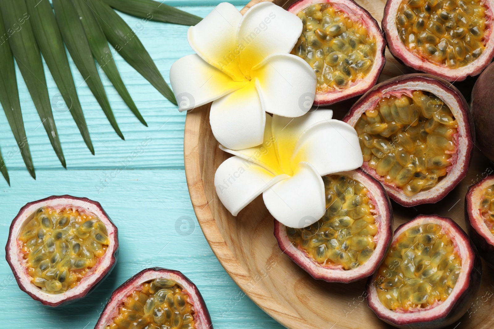 Photo of Halves of passion fruits (maracuyas), palm leaf and flowers on light blue wooden table, flat lay