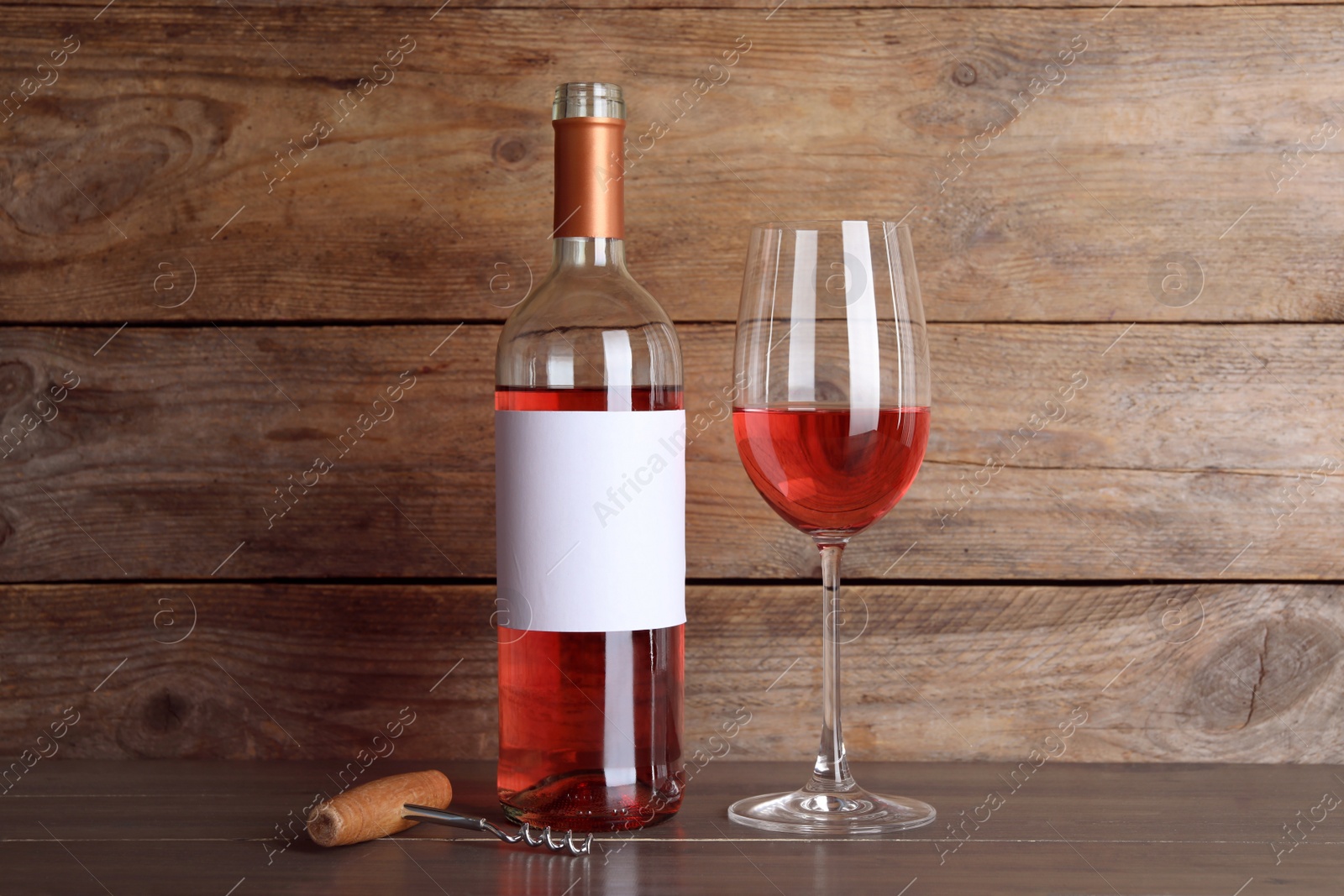 Photo of Corkscrew near bottle and glass of delicious rose wine on table against wooden background