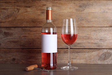 Photo of Corkscrew near bottle and glass of delicious rose wine on table against wooden background