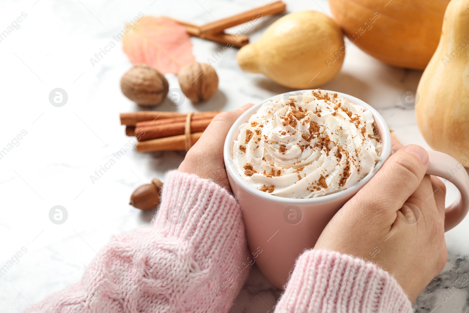 Photo of Woman holding cup with tasty pumpkin spice latte at white marble table, closeup