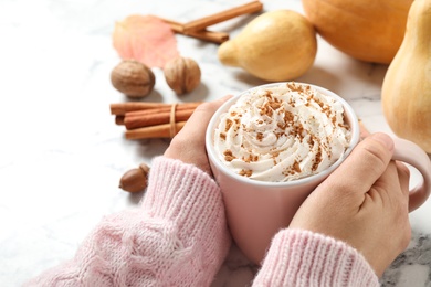 Woman holding cup with tasty pumpkin spice latte at white marble table, closeup