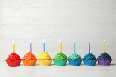 Delicious birthday cupcakes with burning candles on white wooden table