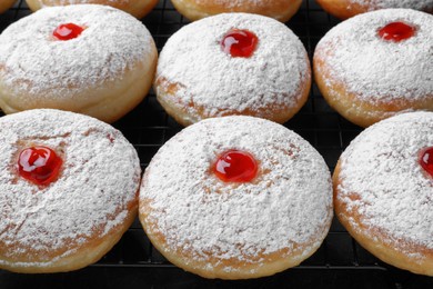 Photo of Many delicious donuts with jelly and powdered sugar on cooling rack, closeup