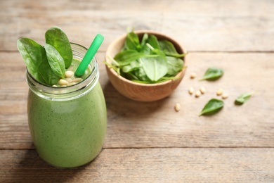 Photo of Jar of healthy green smoothie with fresh spinach on wooden table. Space for text