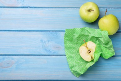 Photo of Apples with beeswax food wrap on light blue wooden table, flat lay. Space for text