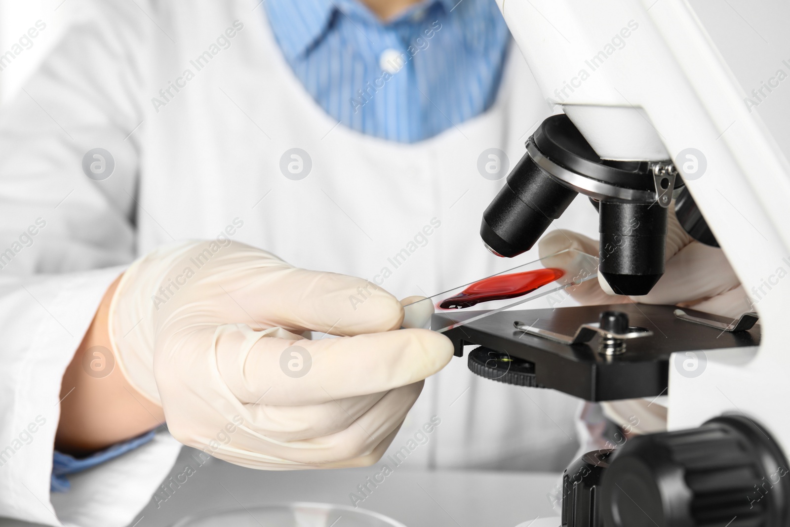 Photo of Scientist holding slide with blood sample near microscope in laboratory, closeup. Virus research