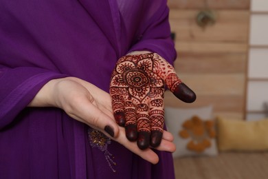 Photo of Woman with henna tattoo on palm indoors, closeup. Traditional mehndi ornament