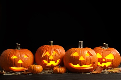 Photo of Pumpkin jack o'lanterns on table in darkness, space for text. Halloween decor