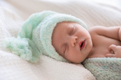 Photo of Cute newborn baby in warm hat sleeping on white plaid, closeup