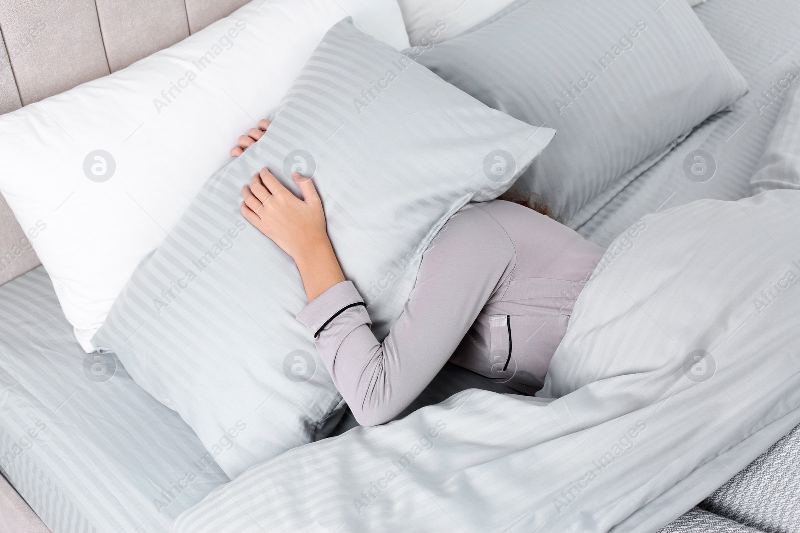 Photo of Young woman covering head with pillow in bed at home, above view