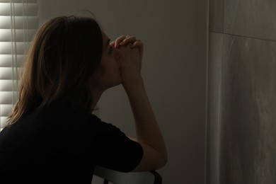 Sad young woman sitting on chair indoors, space for text