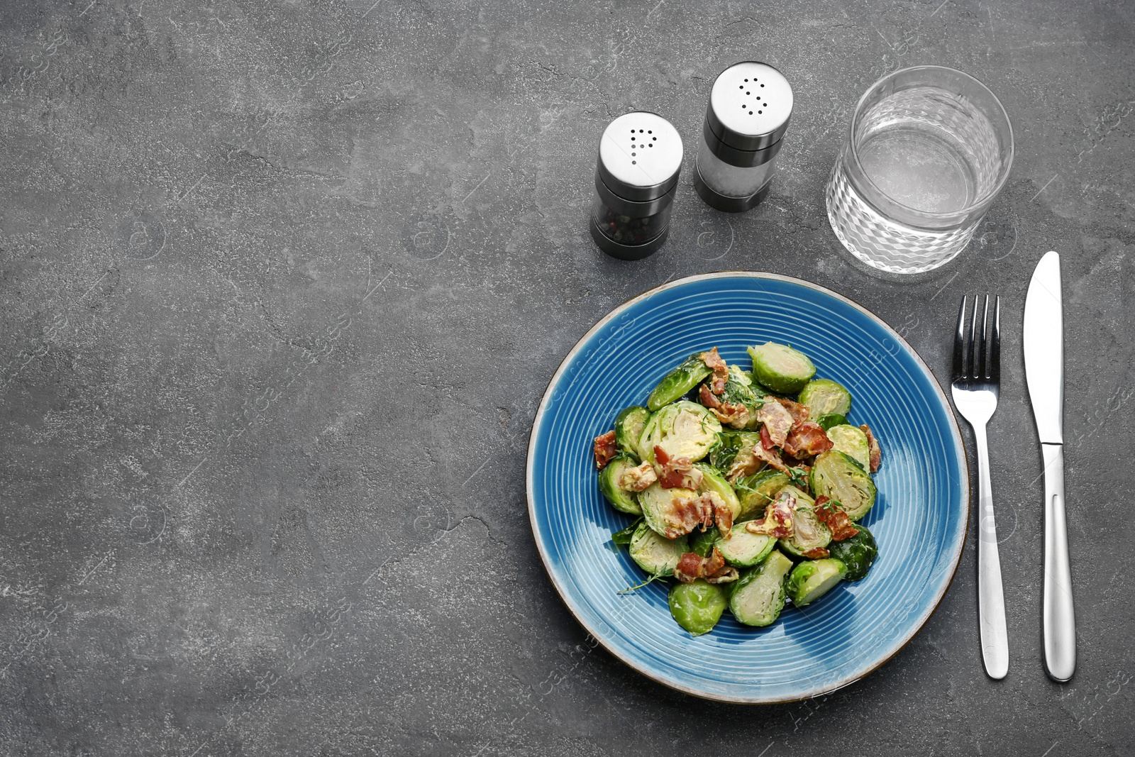 Photo of Delicious cooked Brussels sprouts with bacon served on grey table, flat lay. Space for text