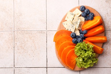 Delicious persimmon, blue cheese and blueberries on tiled surface, flat lay. Space for text