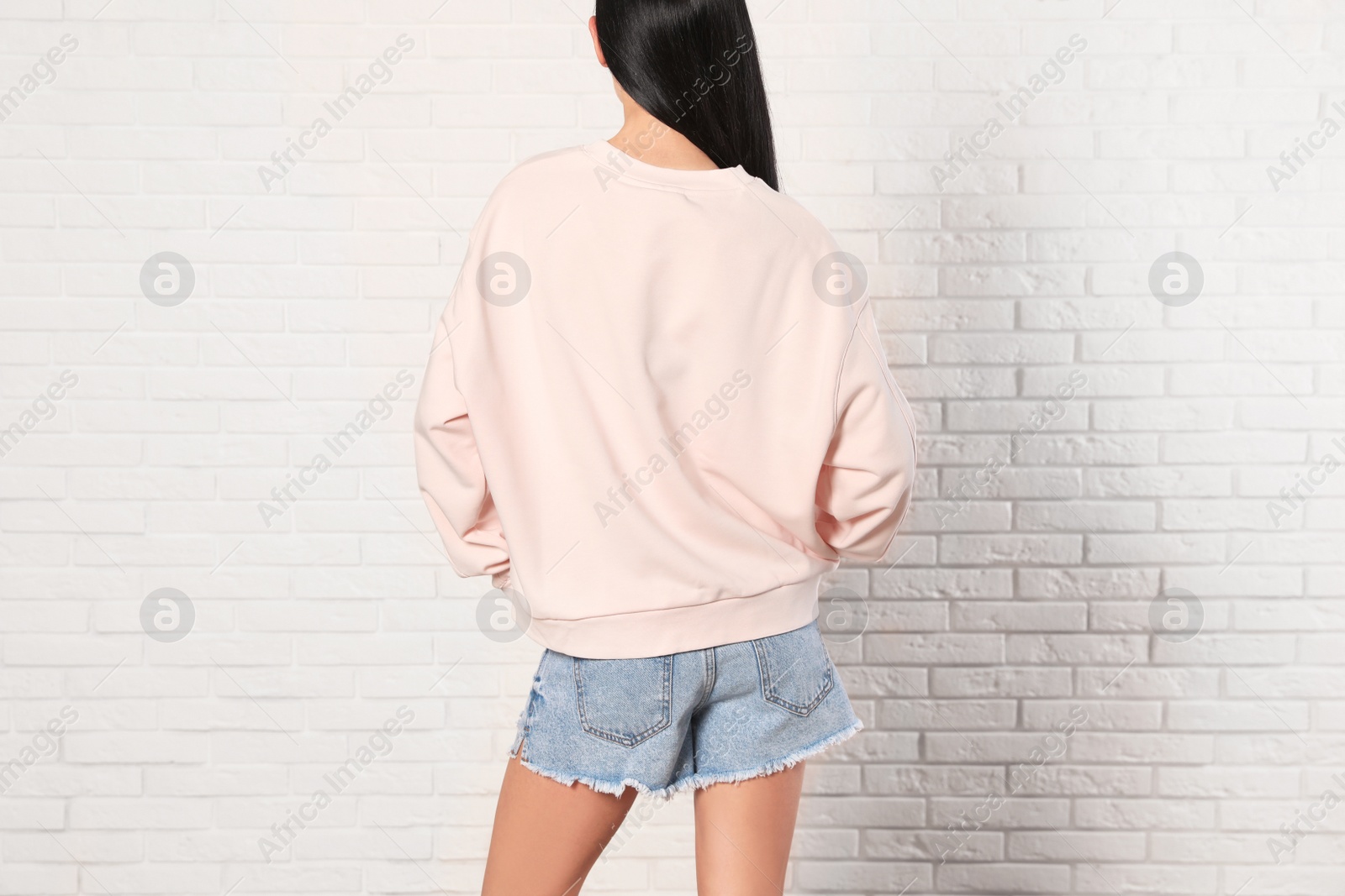 Photo of Young woman in sweater at brick wall, closeup. Mock up for design