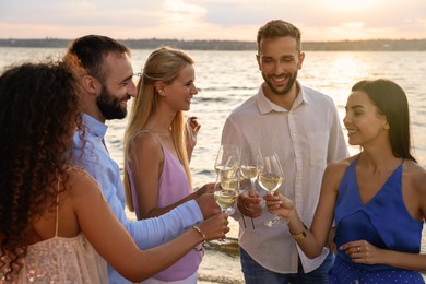 Photo of Friends with glasses of wine having fun near river at summer party