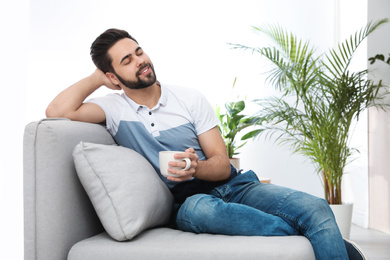 Photo of Young man with cup of drink relaxing on couch at home