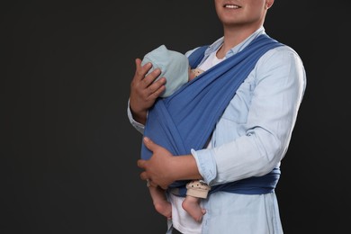 Father holding his child in sling (baby carrier) on black background, closeup. Space for text