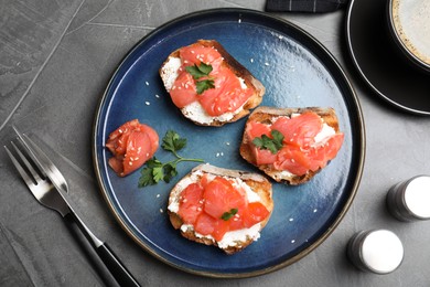 Tasty bruschettas with salmon, cream cheese and parsley on grey table, flat lay