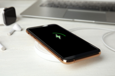 Photo of Mobile phone charging with wireless device on white wooden table, closeup