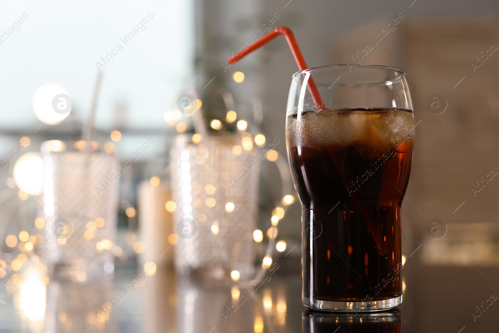 Photo of Glass of cold cola and fairy lights on table. Space for text