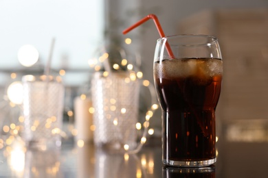 Glass of cold cola and fairy lights on table. Space for text