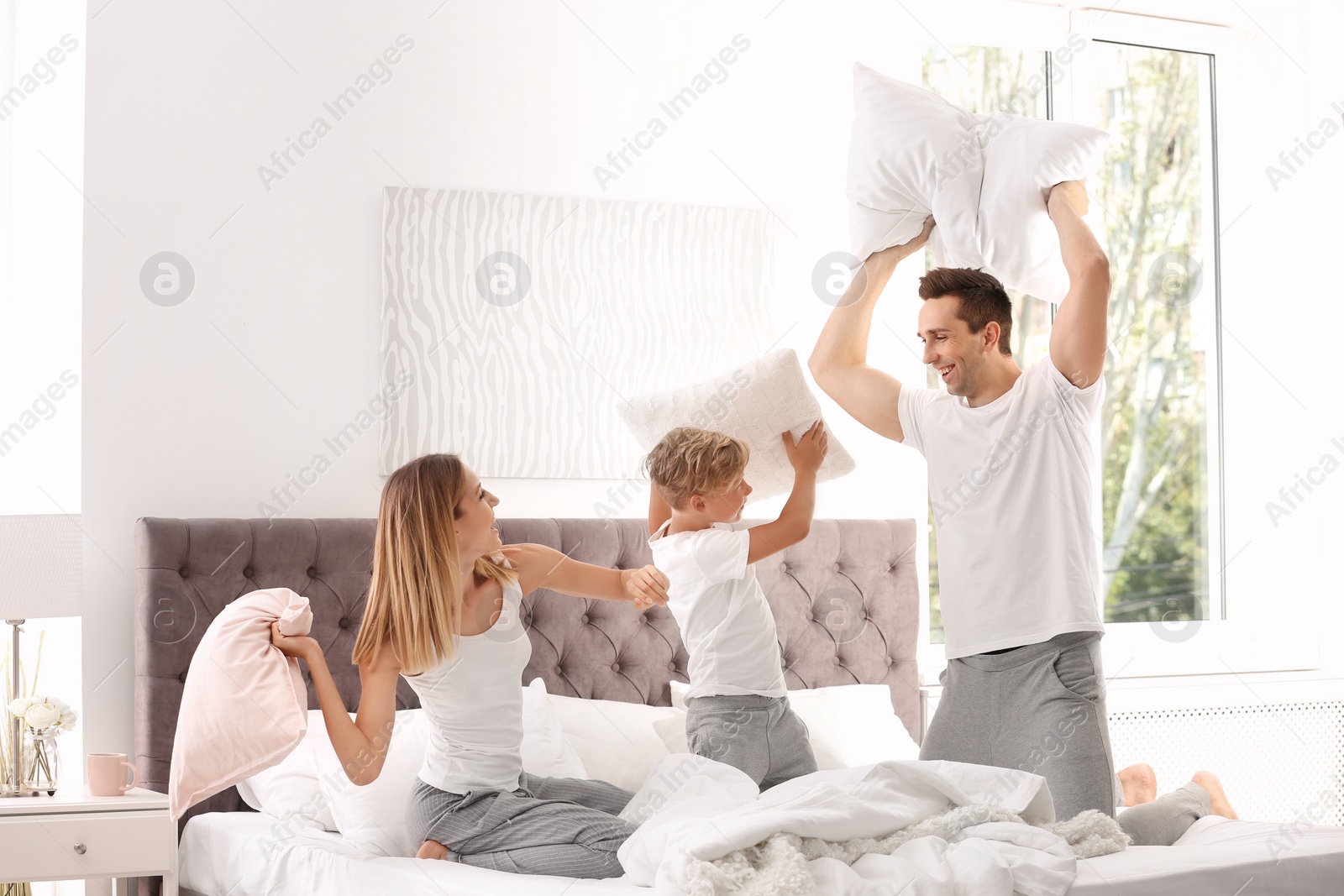 Photo of Happy family having pillow fight on bed at home