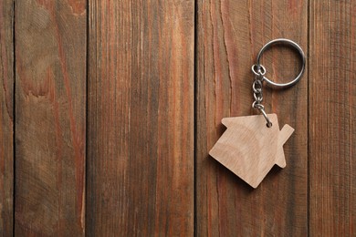 Photo of One keychain in shape of house on wooden table, top view. Space for text